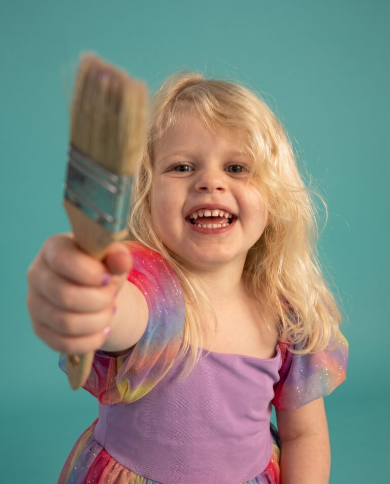 Color Sessions Mini Shooting Trier. Kind mit buntem Pinsel vor türkisem Hintergrund – kreatives Fotoshooting für Kinder.
